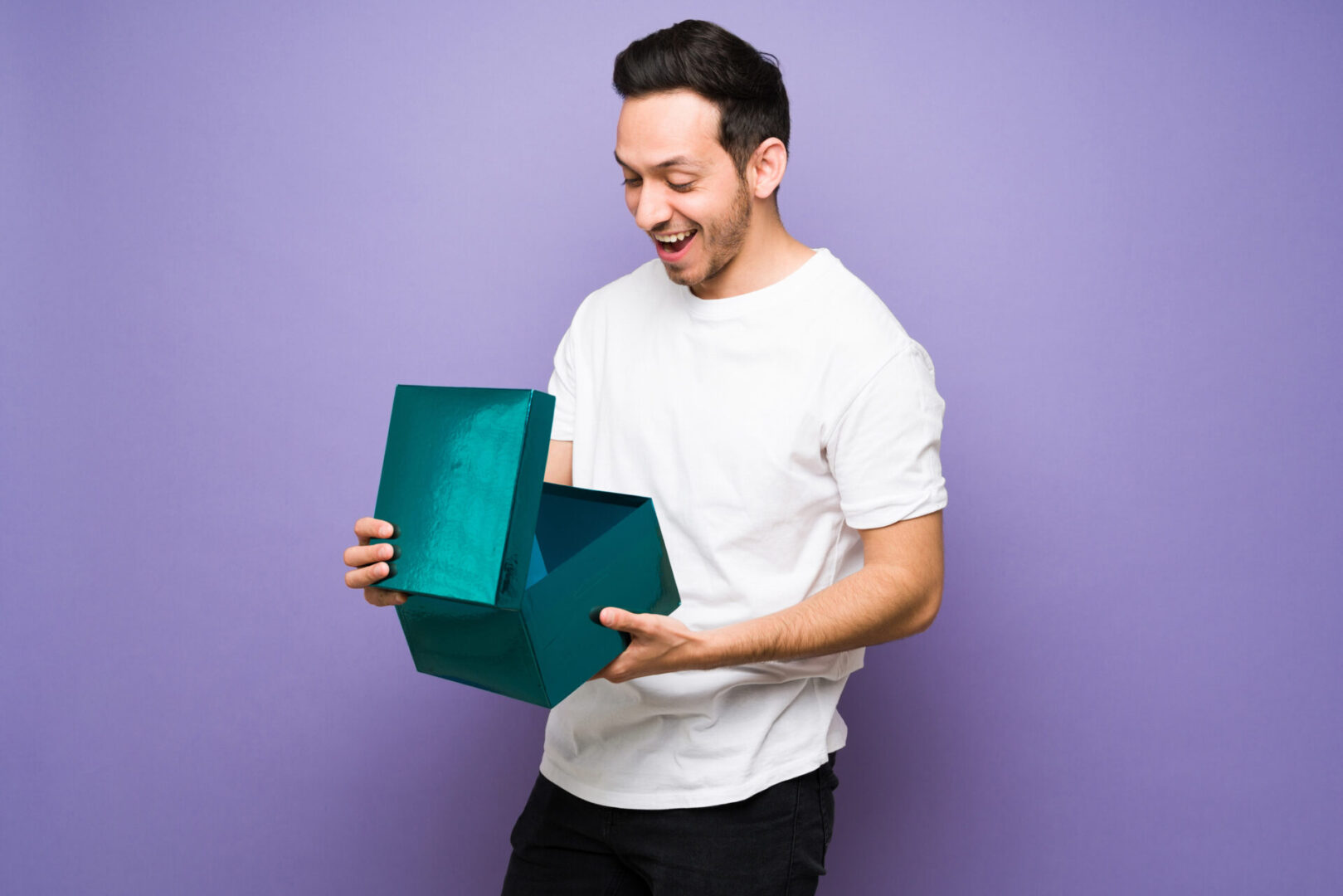 Man excitedly opening a large teal gift box against a purple background.