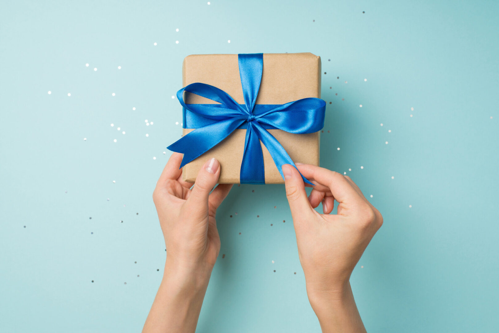 Hands tying a blue ribbon on a small gift box.