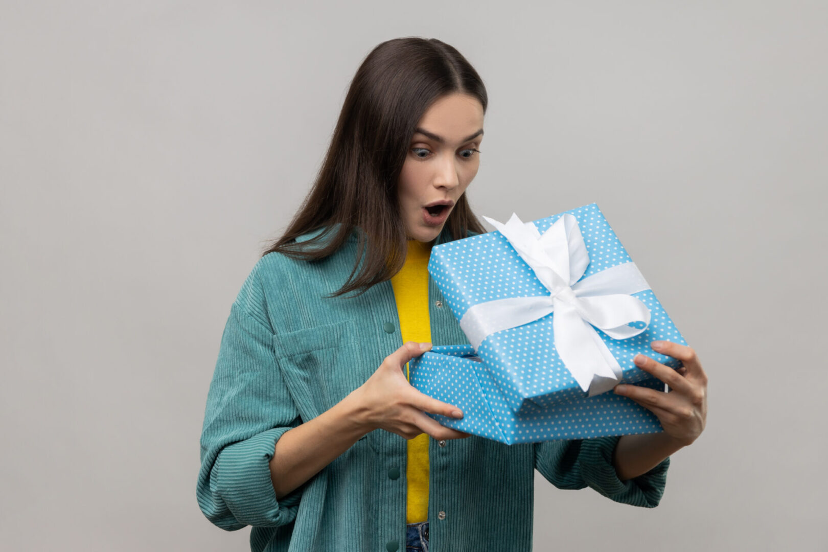 Surprised woman opening a blue gift box with white ribbon.