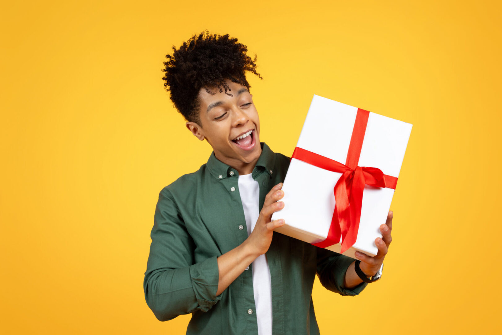 Excited young man holding a gift box with a red ribbon against a yellow background.