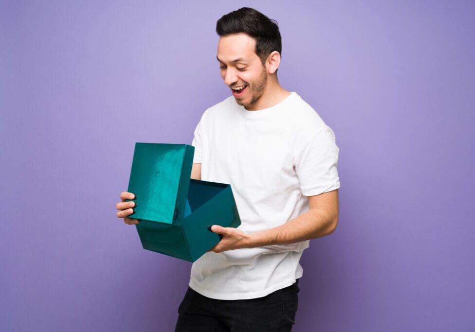 Man excitedly opening a large teal gift box against a purple background.