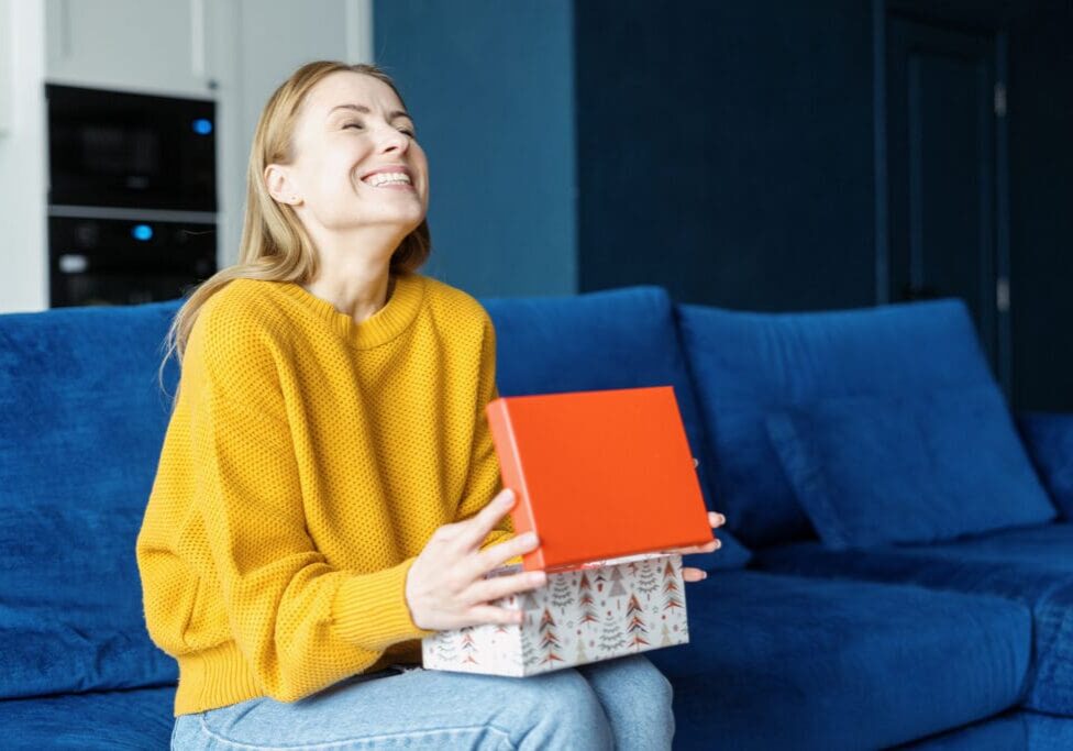 A joyful woman holding a gift box with a red lid.